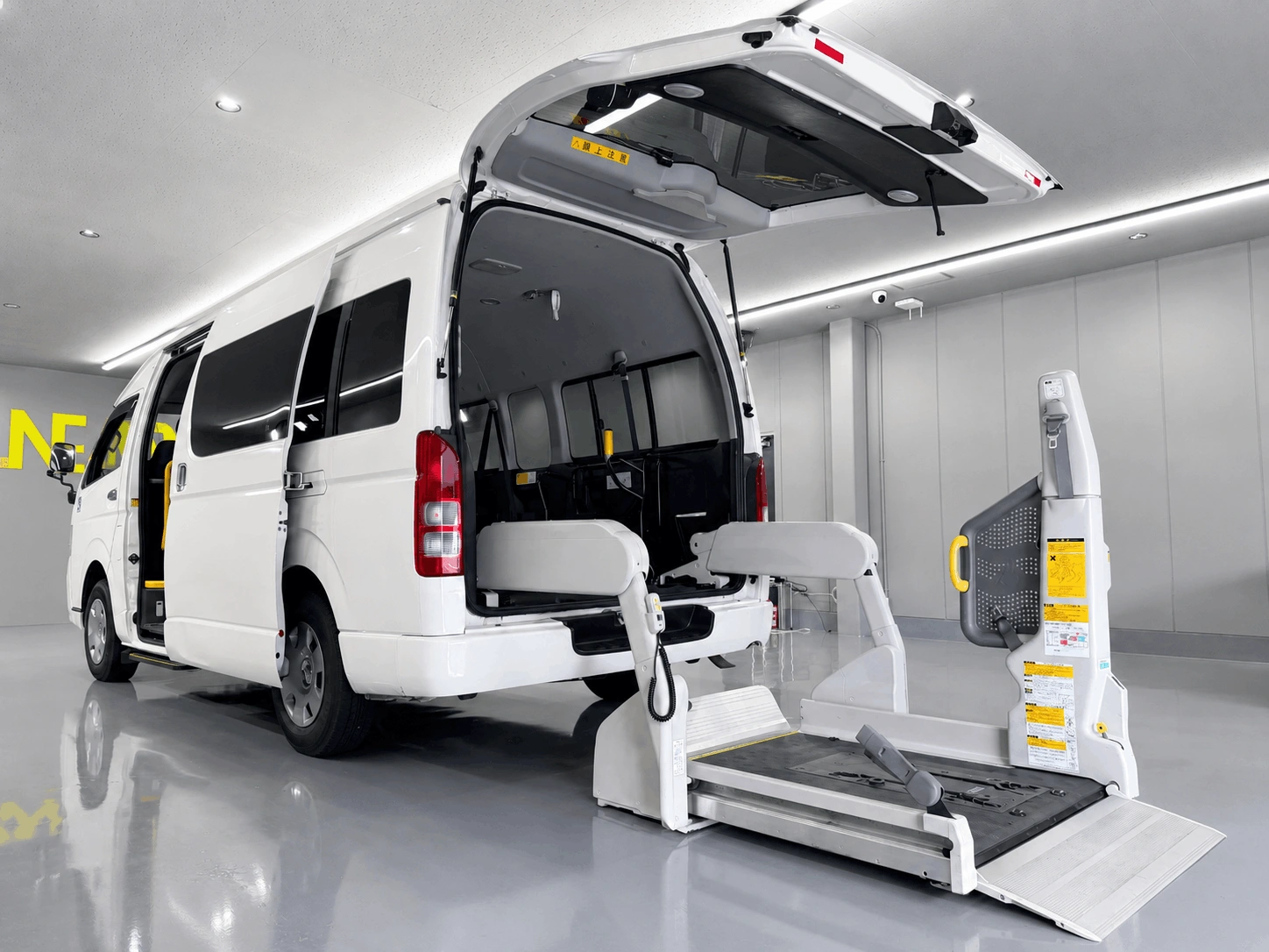 白色のトヨタ・ハイエース（福祉車両仕様）の後部ハッチバックが開いており、車いす用の電動リフトが展開されている写真