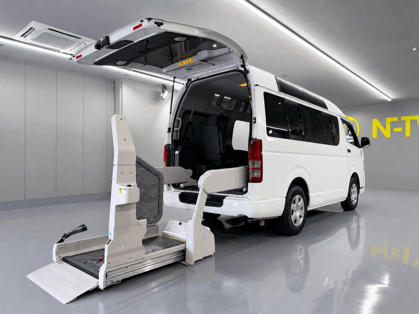 白色のトヨタ・ハイエース（福祉車両仕様）の後部ハッチバックが開いており、車いす用の電動リフトが展開されている写真