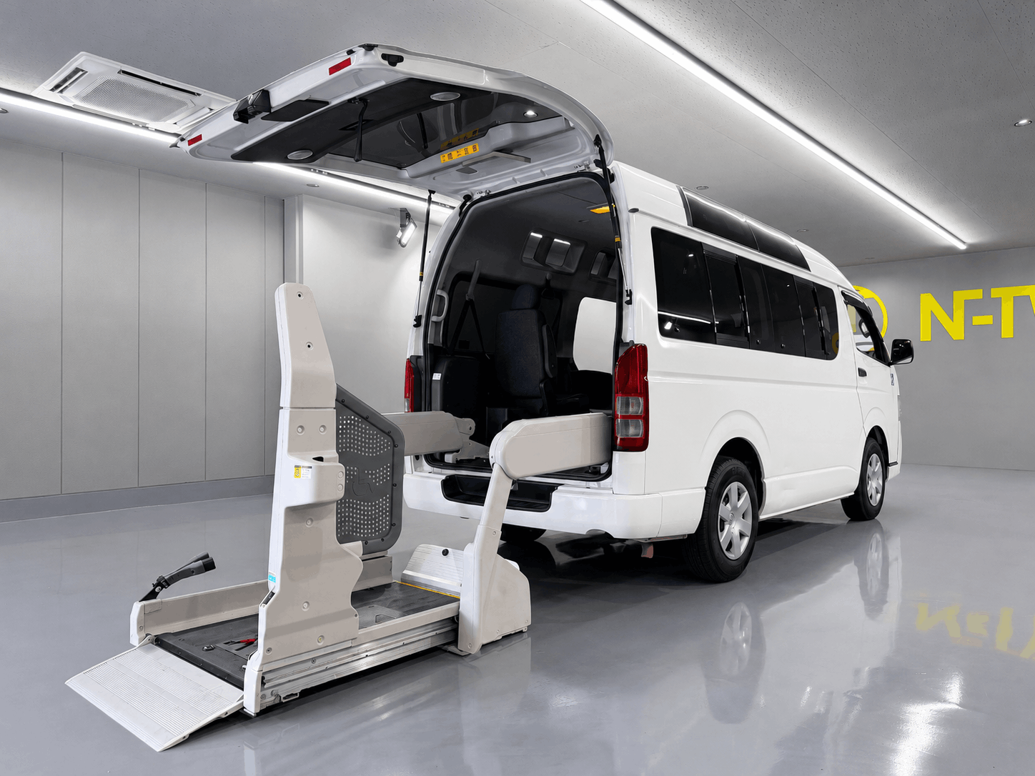 白色のトヨタ・ハイエース（福祉車両仕様）の後部ハッチバックが開いており、車いす用の電動リフトが展開されている写真