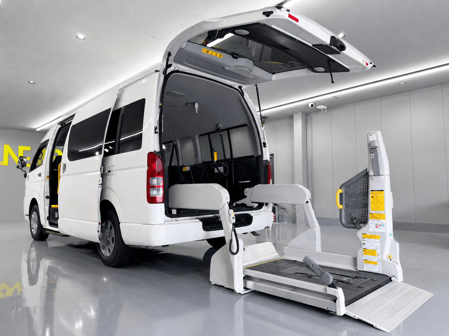 白色のトヨタ・ハイエース（福祉車両仕様）の後部ハッチバックが開いており、車いす用の電動リフトが展開されている写真