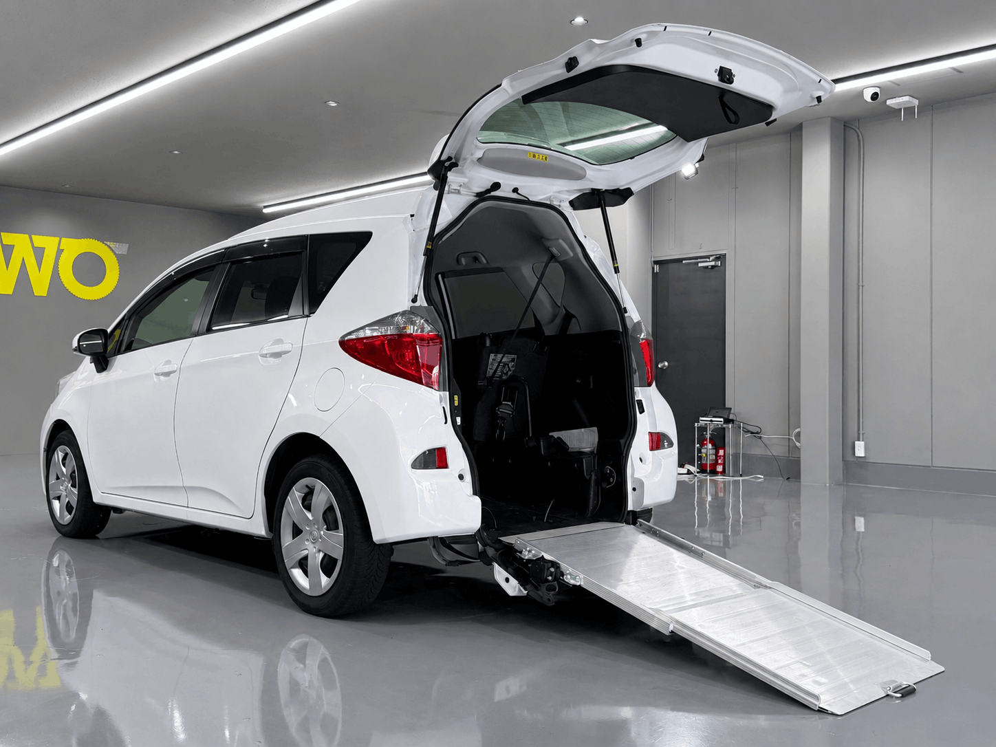 白色のトヨタ・ラクティス（福祉車両仕様）の後部ハッチバックが開いており、車いす用のスロープが展開されている写真